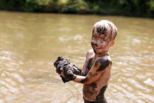 Измазанный грязью мальчик у озера